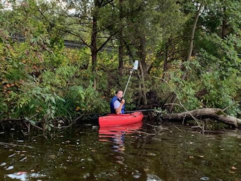 Child in red kayak holding up trash in lake next to treeline